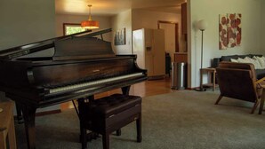 Um piano de cauda numa sala de estar com carpete, um sofá e um candeeiro.