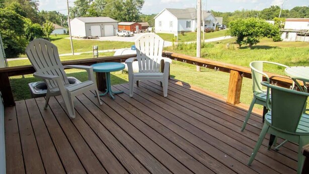 Um deck de madeira com duas cadeiras Adirondack brancas e uma mesa redonda pequena.