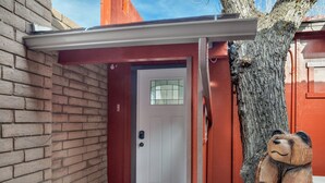 A red door with a white overhang, a tree trunk, and a bear sculpture.