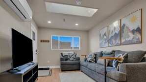 A modern living room with a flat-screen TV, grey sofas, a coffee table, and artwork on the walls.