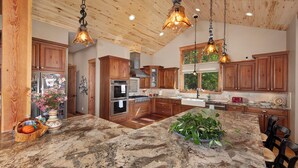 A kitchen with wooden cabinets, granite countertops, and pendant lighting. - Luxury Mountain Home with Private Hot Tub and Stunning Mountain Views (Silverthorne)