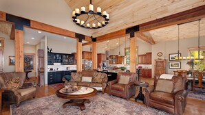 A spacious living room with leather sofas, a coffee table, and a large rug. There is a kitchen in the background with wooden cabinets and a dining area with a table and chairs. - Luxury Mountain Home with Private Hot Tub and Stunning Mountain Views (Silverthorne)