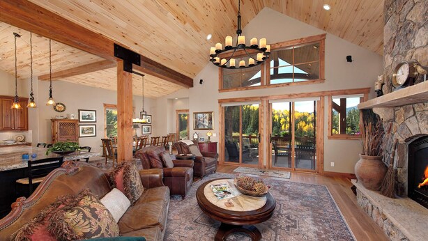A spacious living room with a fireplace, leather sofas, a dining area, and a large window overlooking a deck. - Luxury Mountain Home with Private Hot Tub and Stunning Mountain Views (Silverthorne)