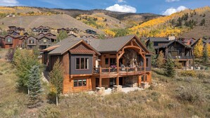 A large wooden house with a balcony, surrounded by other similar houses and a mountainous backdrop. - Luxury Mountain Home with Private Hot Tub and Stunning Mountain Views (Silverthorne)