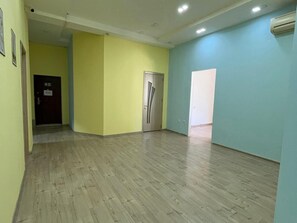 A hallway with wooden flooring, a door, and a wall with a light switch. - Friends Hostel (Baku)
