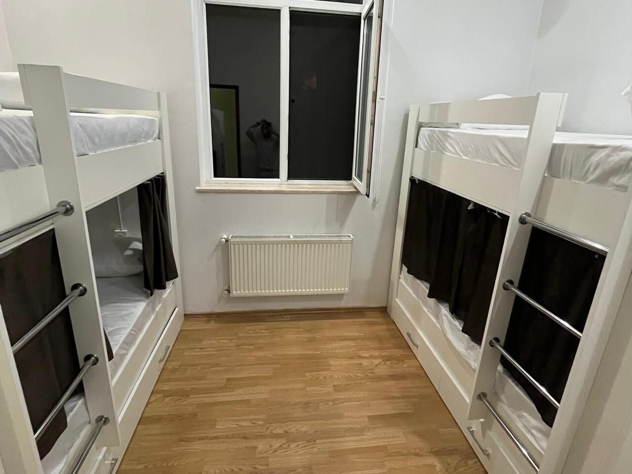 A room with bunk beds, a window, a radiator, and wooden flooring.