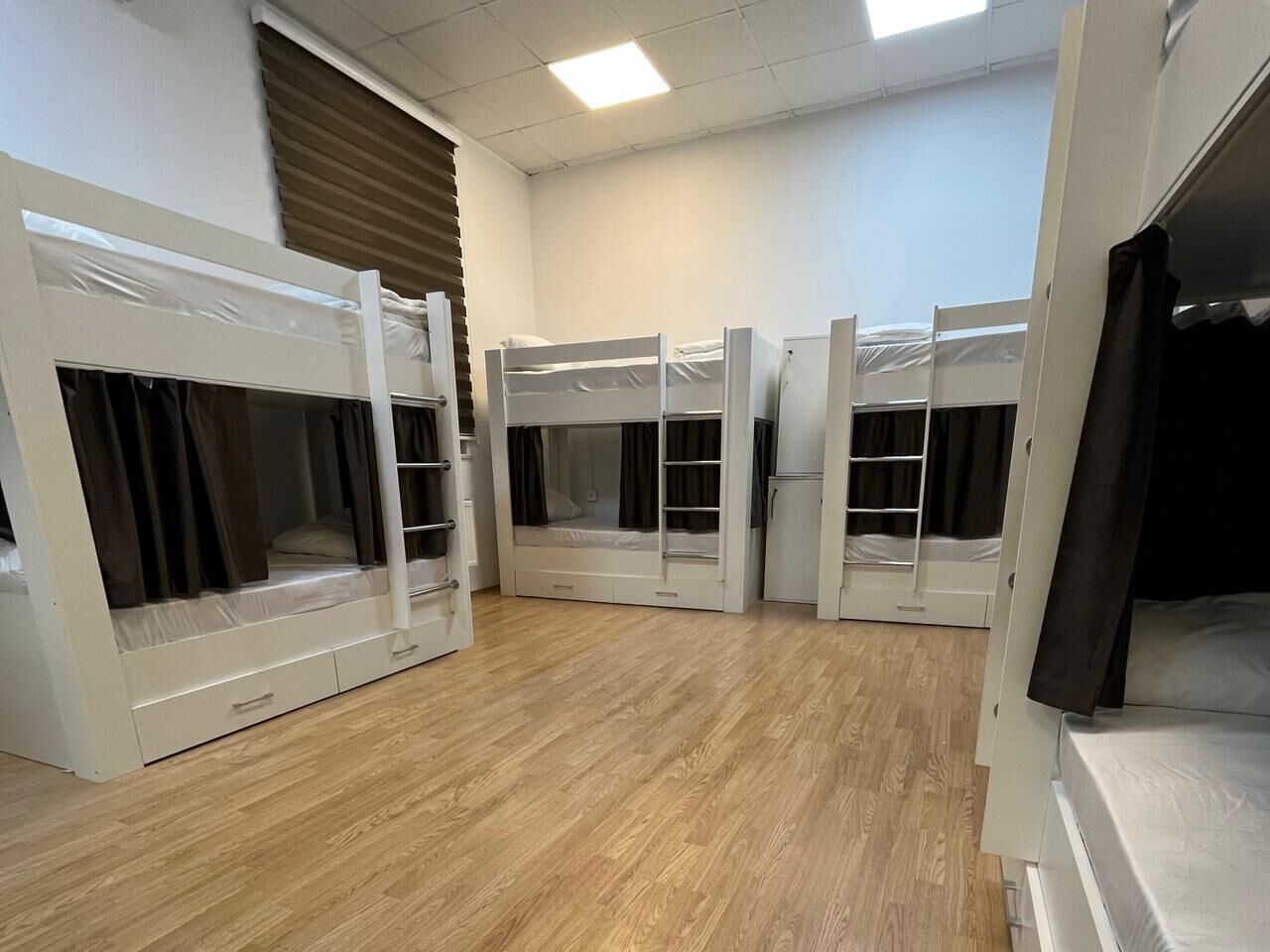 A room with bunk beds, wooden flooring, and a window with blinds.