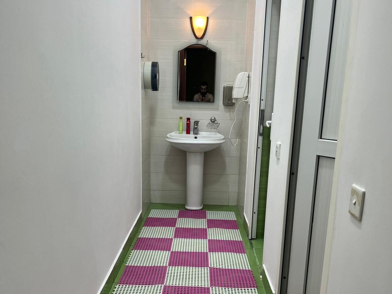 Ein schmales Badezimmer mit einem weißen Waschtisch, einem Spiegel und einem grün-weißen Schachfußboden.
