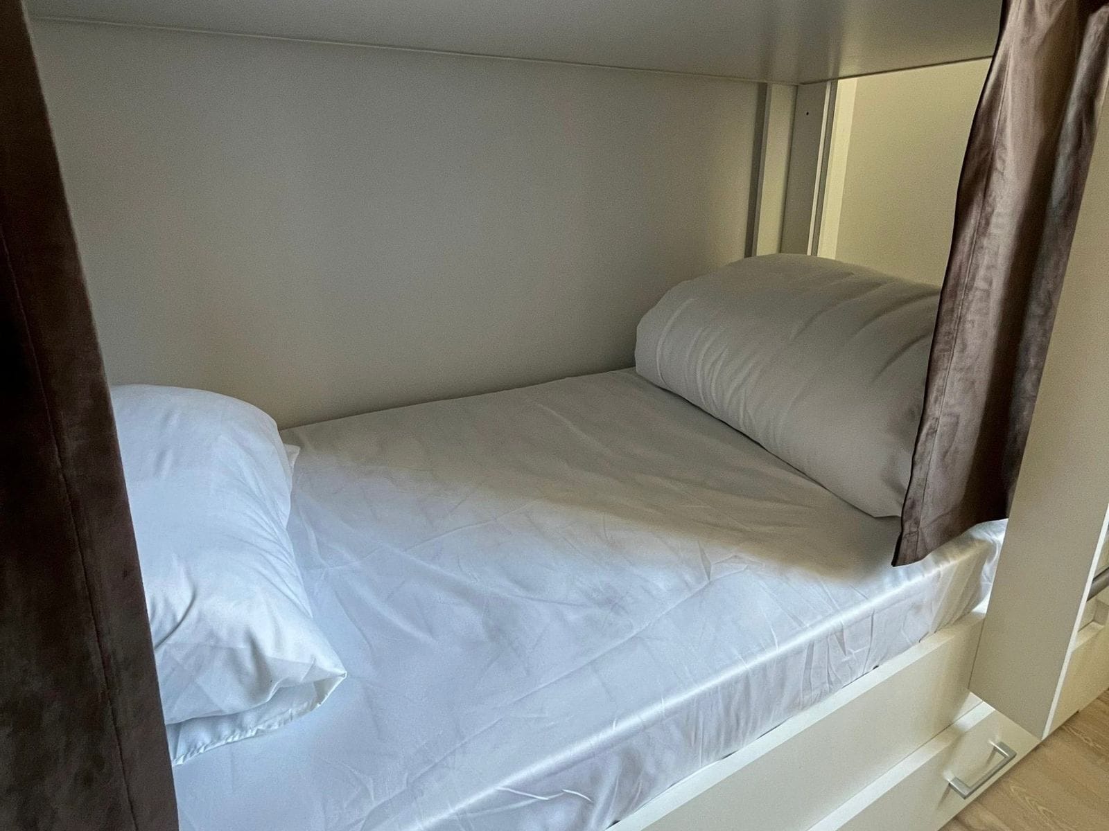 A single bed with white bedding in a room with a plain wall and a wooden floor.