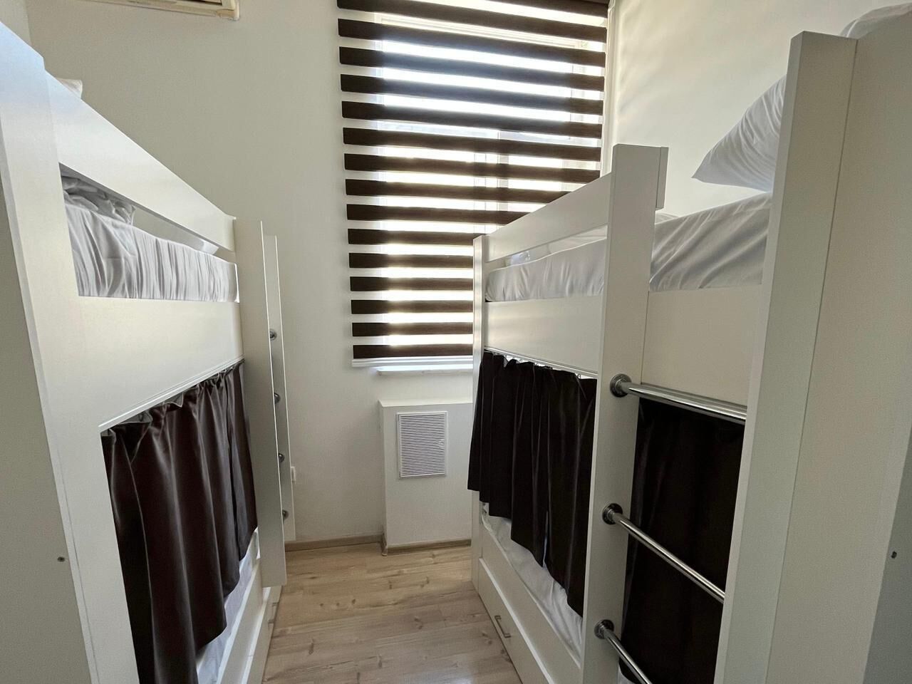 A narrow room with bunk beds, a window with blinds, and a radiator.
