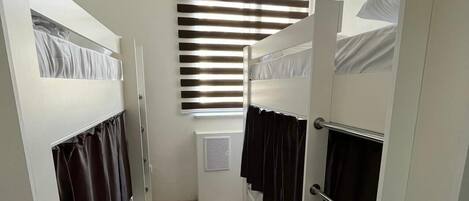 A narrow room with bunk beds, a window with blinds, and a radiator.
