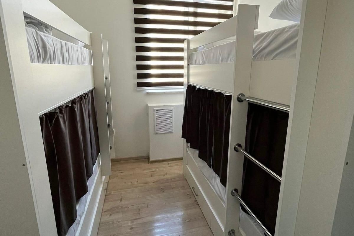 Un couloir avec des lits superposés, un radiateur et une fenêtre avec des stores.