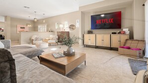 Una sala de estar moderna con un televisor de pantalla plana, un ventilador de techo y una mesa de centro con un libro y un florero.