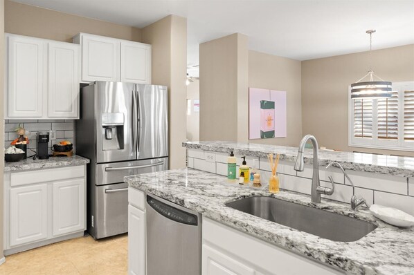 A modern kitchen with white cabinets, stainless steel appliances, a granite countertop, and a built-in dishwasher. - 4BR Estrella Mountain Retreat w/ Heated Pool (Goodyear)