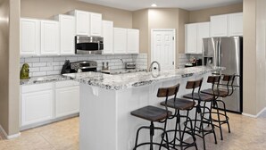 Una cocina moderna con armarios blancos, encimera de granito, electrodomésticos de acero inoxidable y taburetes de bar.
