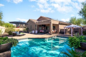 A backyard with a swimming pool, patio furniture, and a covered seating area. - 4BR Estrella Mountain Retreat w/ Heated Pool (Goodyear)