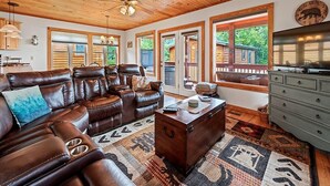 A spacious living room with a leather sectional sofa, a wooden ceiling, large windows, and a television. - Watch the Elk from the Deck! Hot Tub, High Speed Wifi, Paved Access (Maggie Valley)
