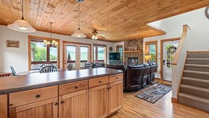 A spacious kitchen with wooden cabinets, a large island, and a fireplace. There are multiple windows providing natural light and a view of the outdoors. - Watch the Elk from the Deck! Hot Tub, High Speed Wifi, Paved Access (Maggie Valley)