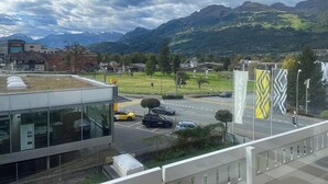 Un edifici modern amb grans finestres, un aparcament i vista a les muntanyes al fons.