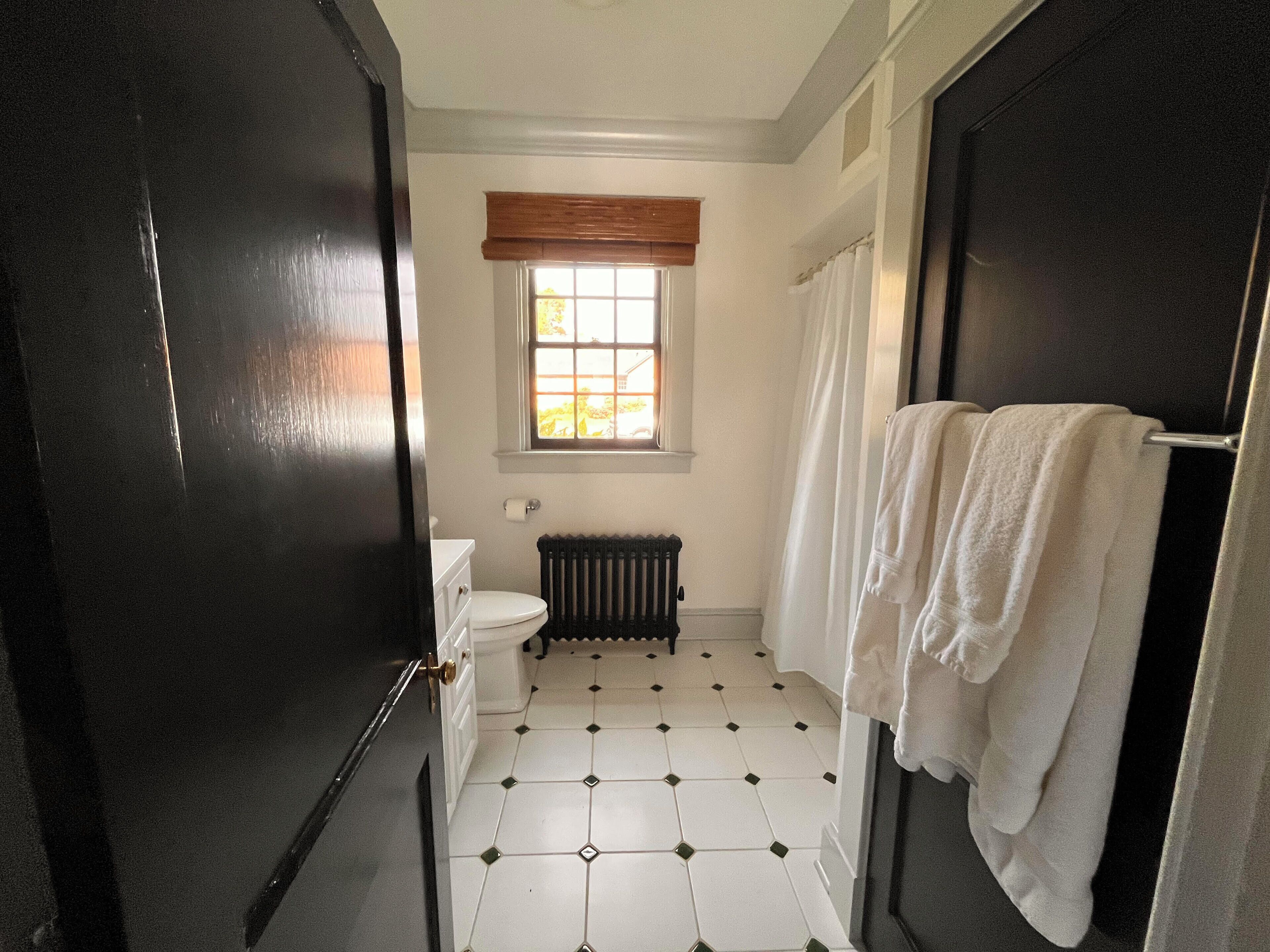 A bathroom with a toilet, a radiator, a window with a wooden blind, and a towel rack with towels.