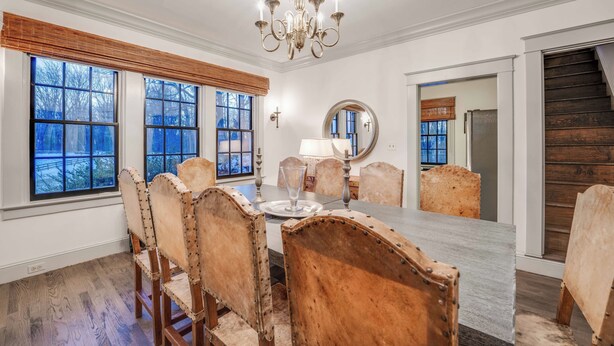 Comedor con una mesa grande, sillas de madera, una araña y ventanas amplias con persianas.