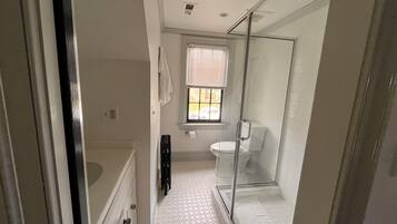A bathroom with a glass shower enclosure, a toilet, and a white tiled floor.