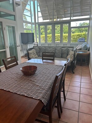Une terrasse ensoleillée avec une table à manger, des chaises, un canapé et un téléviseur.