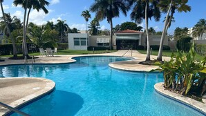 A swimming pool with a clear blue water feature, surrounded by palm trees and a building with a red roof. - Golf & Casino Beach Villa @Dorado del Mar (Dorado)