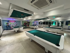 Una sala de billar con varias mesas, sillas y un mural con la figura de un león.