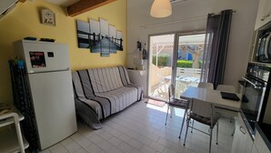 A compact kitchen with a refrigerator, a dining table with chairs, a sofa, and a large window with curtains. - Air-conditioned holiday home for 5 people, secure residence MAS DE LA PLAGE, south-facing... (PORTIRAGNES)