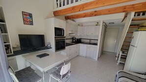 A compact kitchen with a microwave, oven, and sink, a dining area with a table and chairs, and a staircase leading to an upper level. - Air-conditioned holiday home for 5 people, secure residence MAS DE LA PLAGE, south-facing... (PORTIRAGNES)