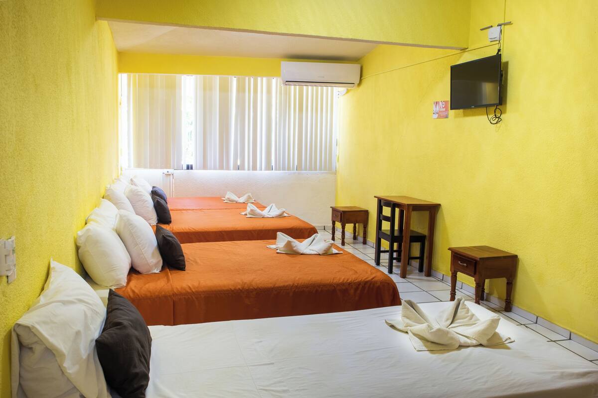 A hotel room with two beds, a TV, a small table, and a window with blinds.