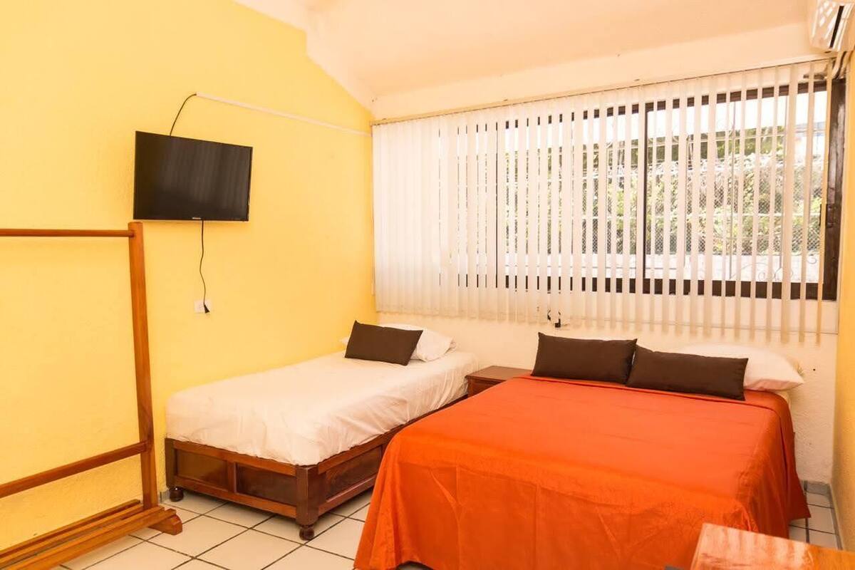 A room with two beds, a TV mounted on the wall, and a window with blinds.