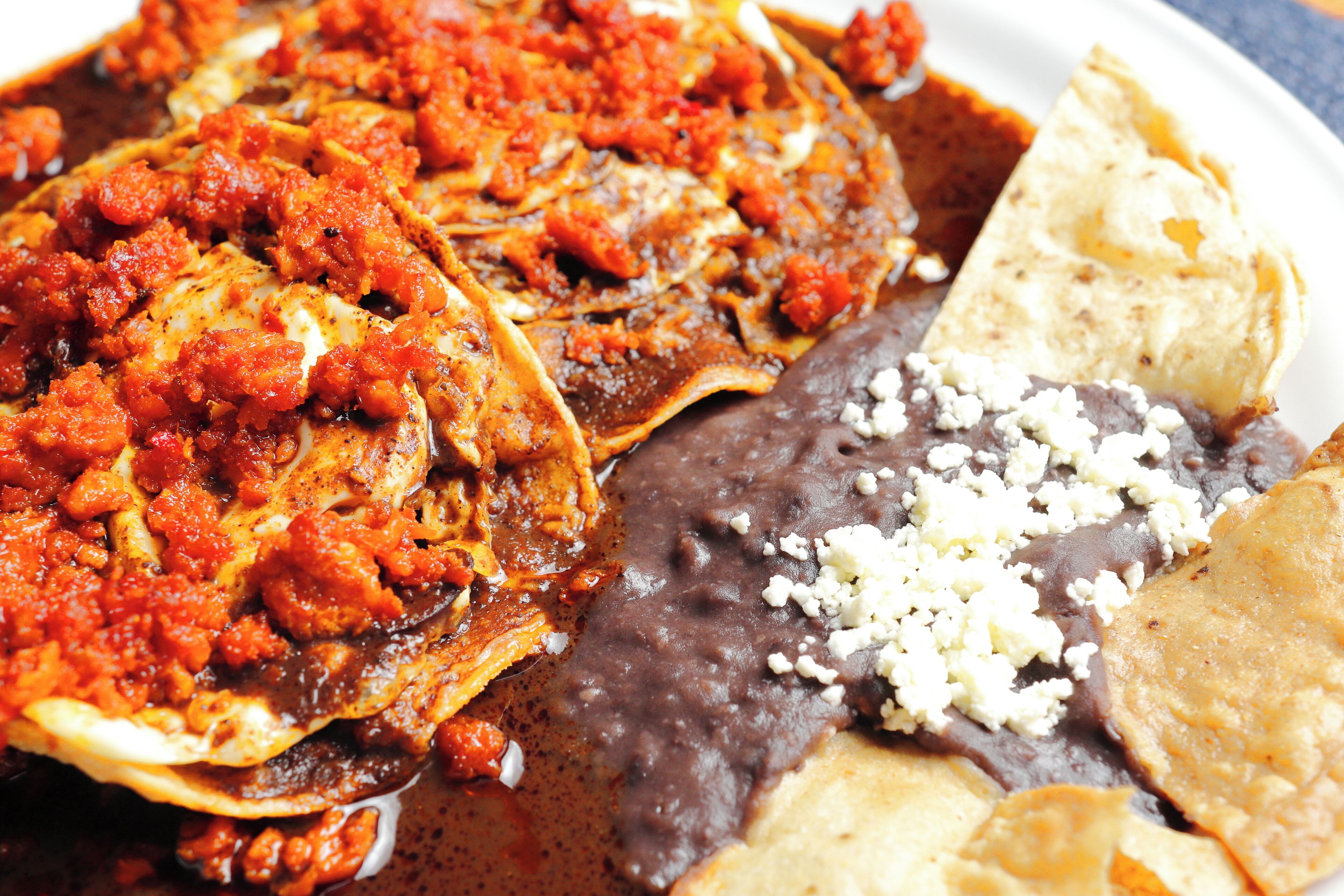 A plate of food with a variety of dishes including a red sauce, beans, and a tortilla.