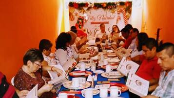Un grupo de personas sentadas alrededor de una mesa con platos, tazas y libros, en una habitación con un ambiente festivo.