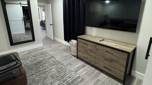 Un salon moderne doté d’un grand téléviseur à écran plat, d’un meuble en bois, d’un tapis gris et d’un miroir qui reflète la pièce.