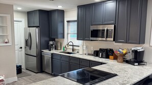 Une cuisine moderne avec des meubles de couleur sombre, des appareils en acier inoxydable, un comptoir en granit et des tabourets de bar noirs.