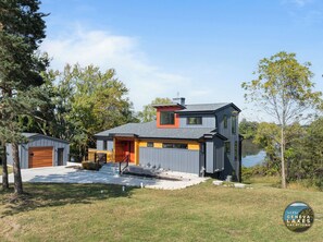 Een modern huis met twee verdiepingen, een garage, een overdekte veranda en uitzicht op een meer.