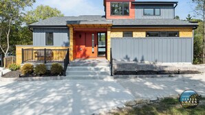 Ett modernt hus i två våningar med ett grått tak, en röd dörr och en grå garagedörr.