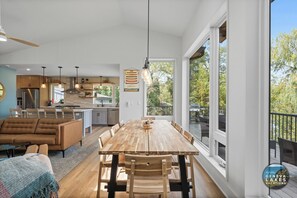 Een ruime keuken met moderne apparatuur, een eethoek met houten tafels en stoelen, en grote ramen met uitzicht op de omgeving.