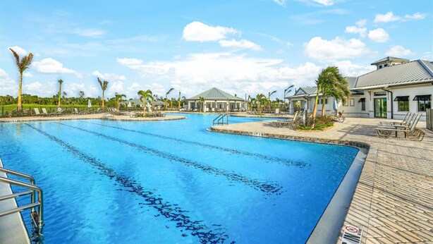 A swimming pool with multiple lanes, surrounded by lounge chairs and palm trees. - 27-night min 3 bdrm 2nd  Heritage Landing Social Transfer Included! (Punta Gorda)