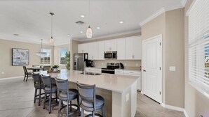 A modern kitchen with white cabinets, stainless steel appliances, and a central island with bar stools. - 27-night min 3 bdrm 2nd  Heritage Landing Social Transfer Included! (Punta Gorda)