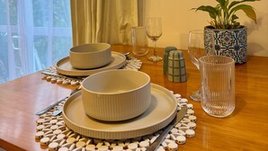 Une table à manger avec des assiettes, des bols et des couverts, un verre et une plante en pot.