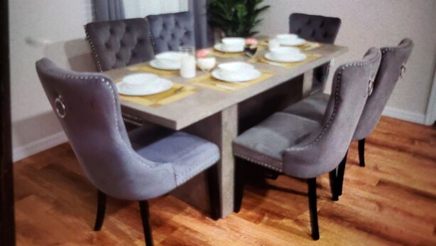 Une table à manger dressée avec des assiettes, des verres et des couverts, entourée de chaises rembourrées aux pieds en métal.