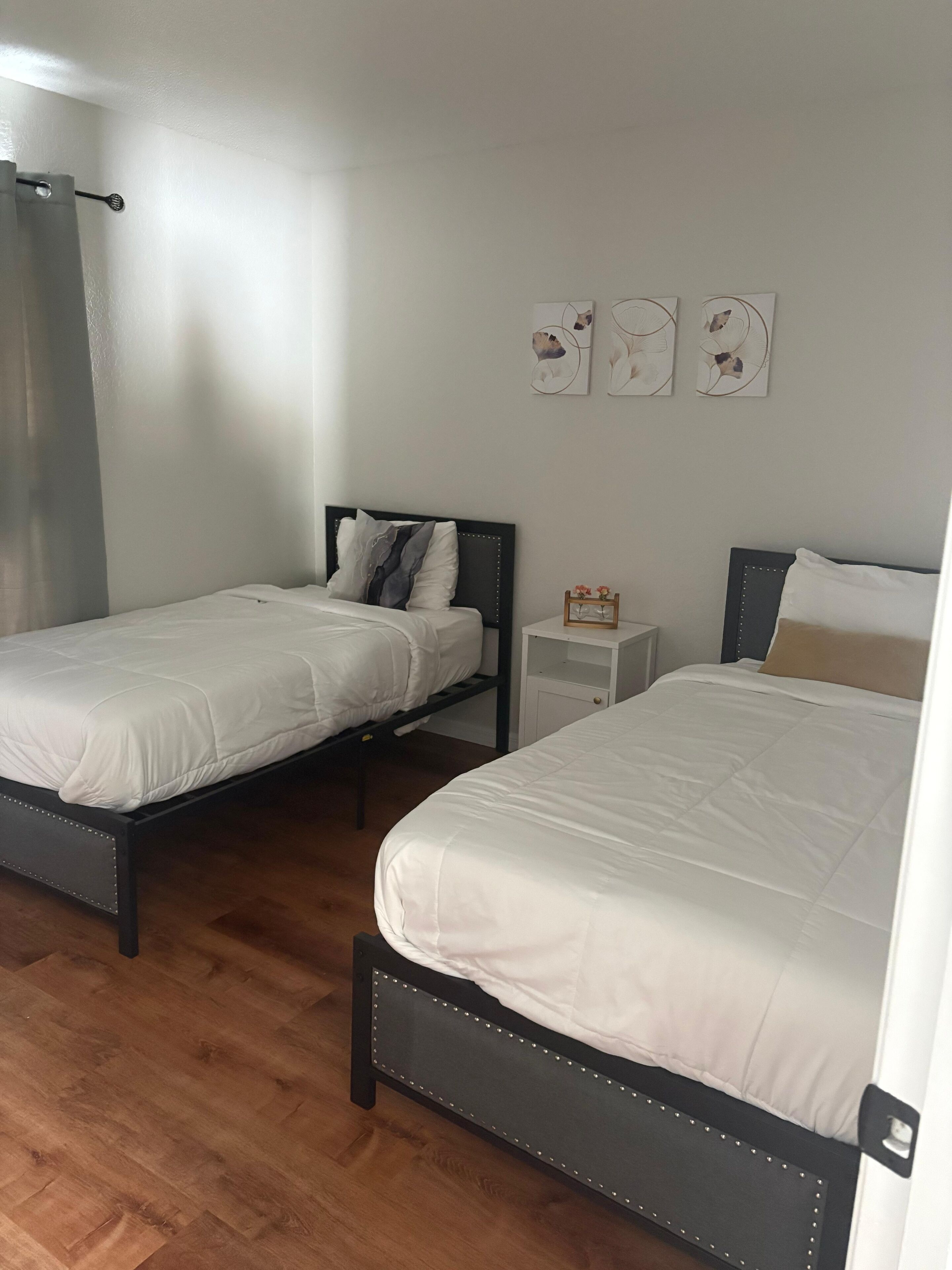 A bedroom with two single beds, a nightstand, and a wall-mounted shelf.