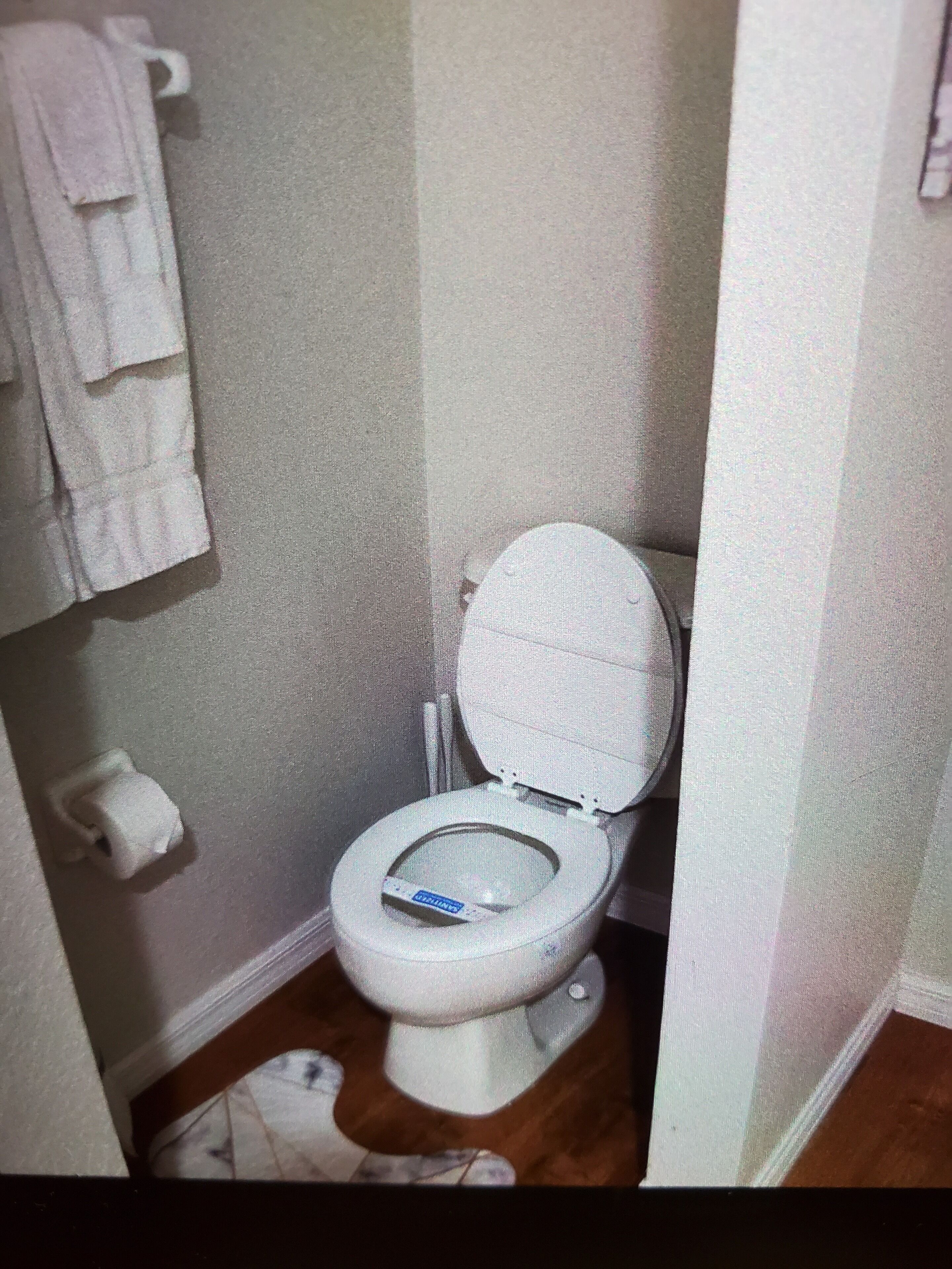 A small bathroom with a toilet, a roll of toilet paper, and a towel rack.