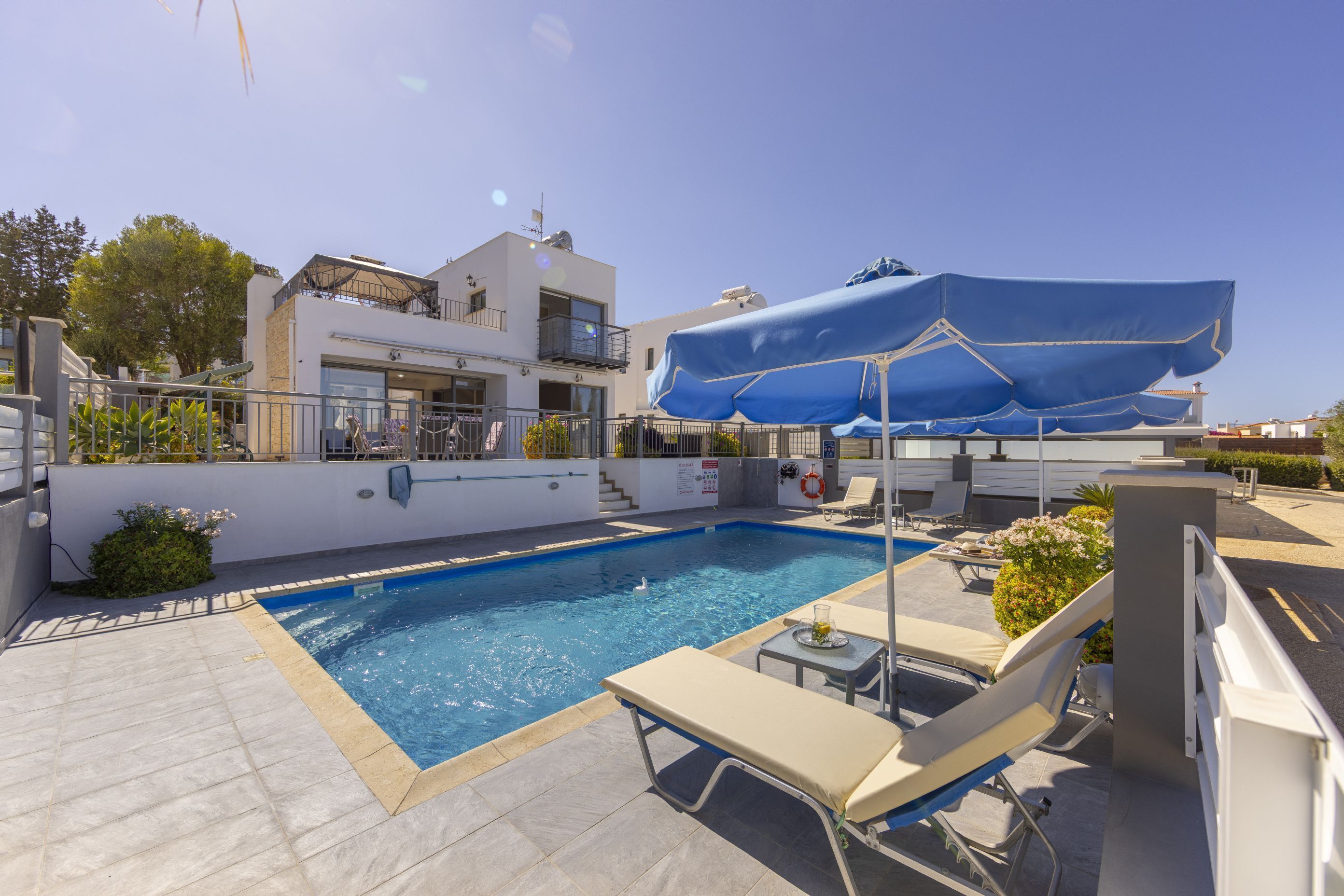 Une piscine entourée de chaises longues et de parasols, le tout bordé par un bâtiment doté d’un balcon et d’un escalier.