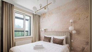 Ein modernes Hotelzimmer mit einem großen Bett, beigen Vorhängen, Blick auf Grünfläche und einer strukturierten Wand.