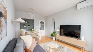 A modern living room with a sofa, TV, and a dining area with chairs and a table.