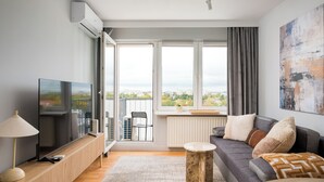 A modern living room with a large window, a flat-screen TV, a sofa, a coffee table, and a side table with a lamp.